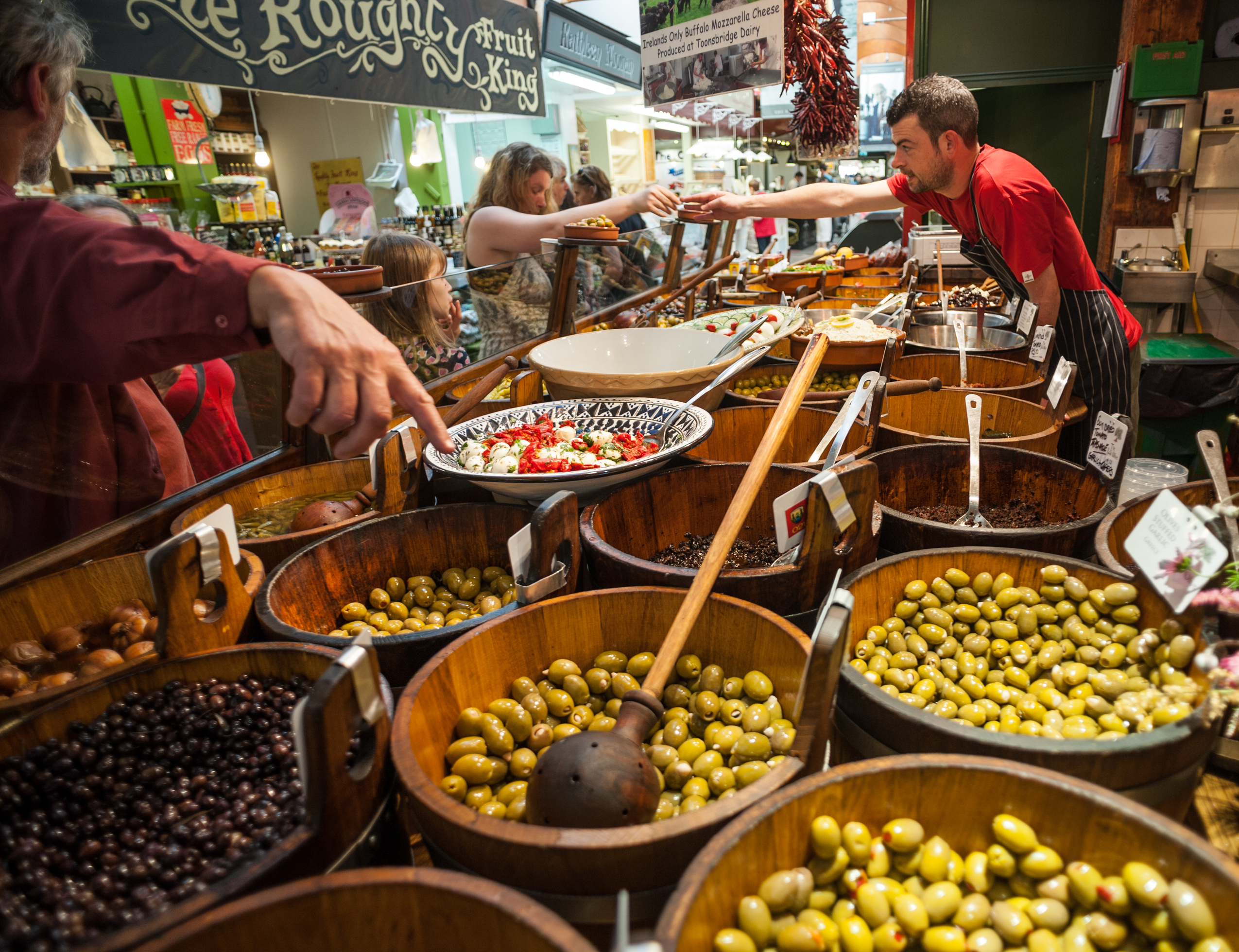 Trader offering a tasting to customers beside barrels of olives at On the Pig's Back in Cork's English Market.
